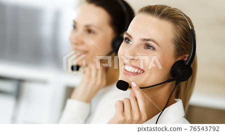 Blond female customer service representative and her colleague are consulting clients online using headset. Call center and business people concept Blond female customer service representative and her colleague are consulting clients online using headset. Call center and business people concept 76543792
