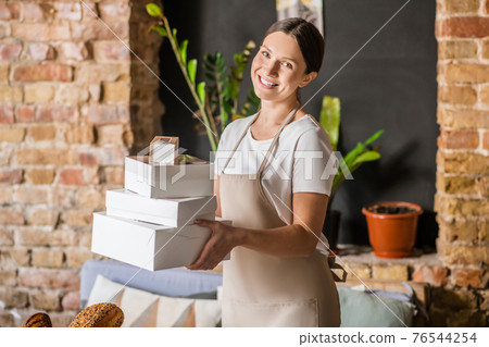Young adult woman in apron with boxes Young adult woman in apron with boxes 76544254