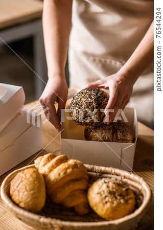 Caring female hand with bread bun over packaging Caring female hand with bread bun over packaging 76544294