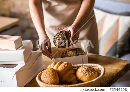 Female hands packing bread bun into box Female hands packing bread bun into box 76544308