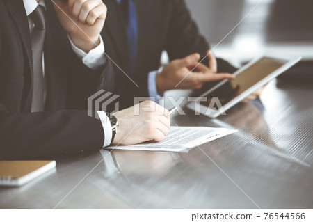 Unknown businessmen using tablet computer and work together at the glass desk in modern office, close-up. Teamwork and partnership concept 76544566