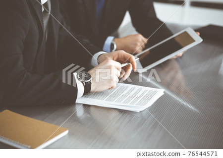 Unknown businessmen using tablet computer and work together at the glass desk in modern office, close-up. Teamwork and partnership concept 76544571