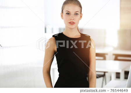 Young blond businesswoman dressed in black dress looks perfect in sunny modern office. Business people concept 76544649