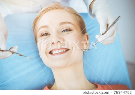 Happy woman is being examined by dentist at dental clinic. Healthy teeth and medicine, stomatology concept 76544792