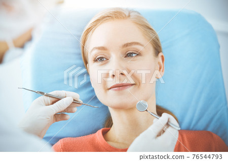 Happy woman is being examined by dentist at dental clinic. Healthy teeth and medicine, stomatology concept 76544793