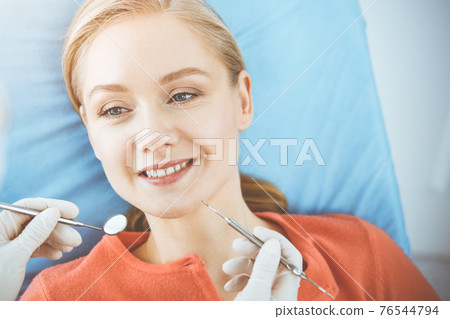 Happy woman is being examined by dentist at dental clinic. Healthy teeth and medicine, stomatology concept 76544794