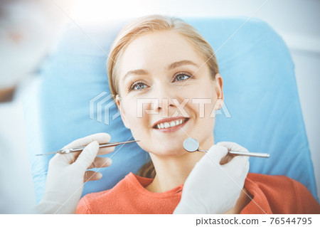 Happy woman is being examined by dentist at dental clinic. Healthy teeth and medicine, stomatology concept 76544795