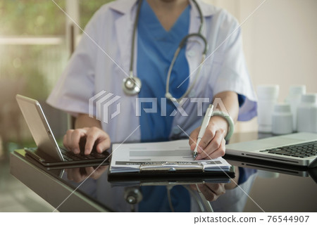 Doctor sitting at table and writing on a document report in hospital office. Medical healthcare staff and doctor service. 76544907