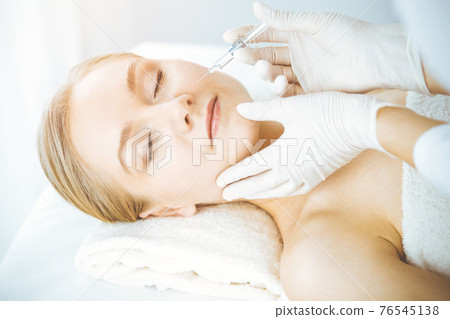 Beautician doctor doing beauty procedure with syringe to caucasian woman. Cosmetic medicine and surgery, beauty injections concept 76545138