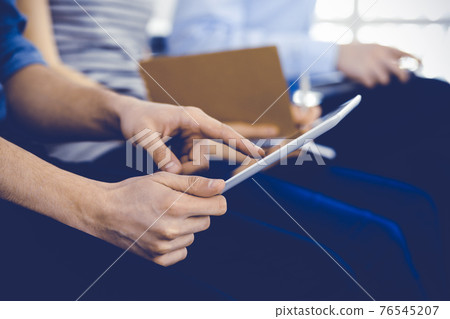 Group of casual dressed business people working at meeting or conference, close-up of hands. Businessman using tablet computer. Teamwork or coaching concept Group of casual dressed business people working at meeting or conference, close-up of hands. Businessman using tablet computer. Teamwork or coaching concept 76545207