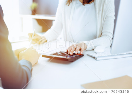 Accountant checking financial statement or counting by calculator income for tax form, hands closeup. Business woman sitting and working with colleague at the desk in office. Tax and Audit concept 76545346