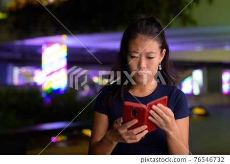 Portrait of beautiful Asian woman outdoors at night using mobile phone Portrait of beautiful Asian woman outdoors at night using mobile phone 76546732