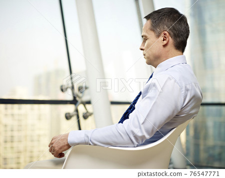 caucasian business executive sitting by the window in a chair thinking in office 76547771