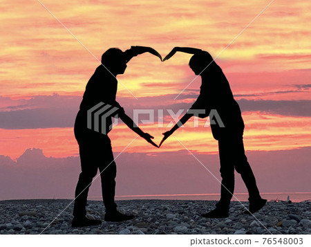 Couple silhouette up that forms a heart in the sea with a superb view of the sunset 76548003