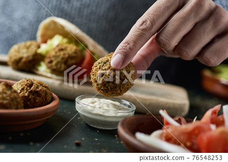 man dipping a falafel in a yogurt sauce 76548253