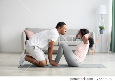 Athletic black couple exercising together at home, working on abs 76548920