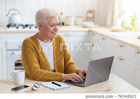 Cheerful elderly woman sitting in front of laptop, taking notes Cheerful elderly woman sitting in front of laptop, taking notes 76548921