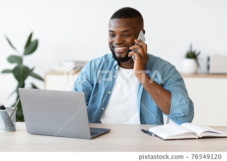 Remote Job. Black Freelancer Guy Using Cellphone And Laptop At Home Office 76549120
