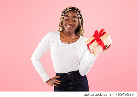 Happy black woman holding present box and thinking Happy black woman holding present box and thinking 76549580