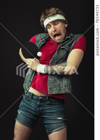 Young Caucasian funny man playing ping pong isolated on black background. Young Caucasian funny man playing ping pong isolated on black background. 76549733