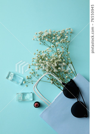 Bag, sunglasses, perfumes, lipstick and flowers on blue background Bag, sunglasses, perfumes, lipstick and flowers on blue background 76550945