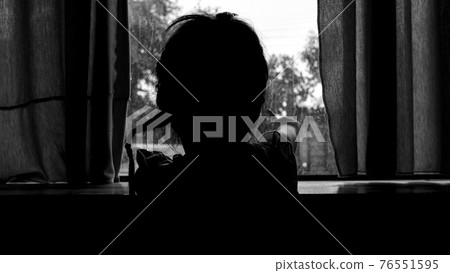 Rear silhouette of sad little girl looking outside through the window in the rainy day. 76551595