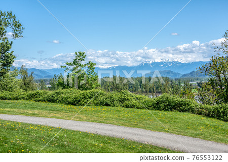 Riverbank walkway with overview of snow caps on Rocky mountains 76553122