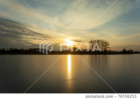 Sunset over a frozen lake with trees on the shore 76556253