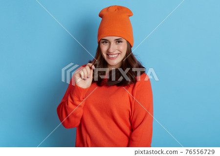 European woman looking playful at camera and touching her hair, wearing casual clothing and cap, has flirting facial expression, feels positive emotions, being satisfied. 76556729