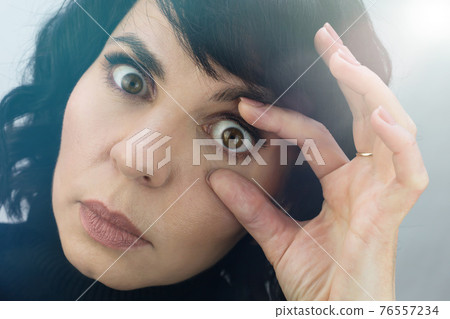 Woman opens her eyes with her fingers for inspection, close-up 76557234