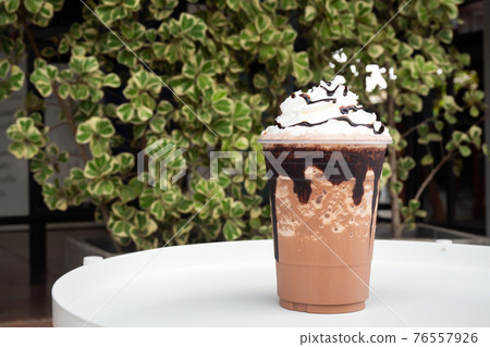 Mocha  frappe in plastic cup with whipping cream and chocolate sauce topping. 76557926