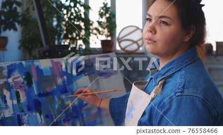A woman artist drawing a painting and looking to the side A woman artist drawing a painting and looking to the side 76558466