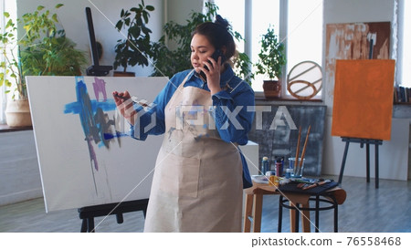A woman paint artist talking in her phone while drawing a painting A woman paint artist talking in her phone while drawing a painting 76558468