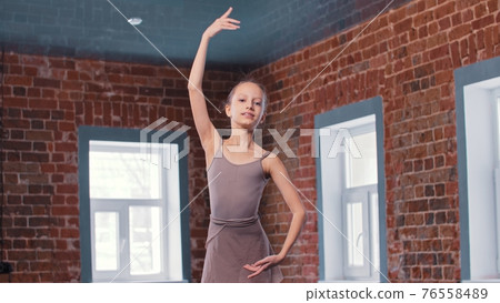 A little skinny ballerina girl training movements in the studio - looking in the camera 76558489