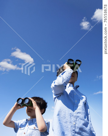 A boy looking through binoculars under the blue sky 76558678