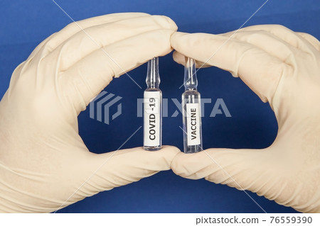 Hands in medical gloves hold vials of the Covid-vaccine 76559390