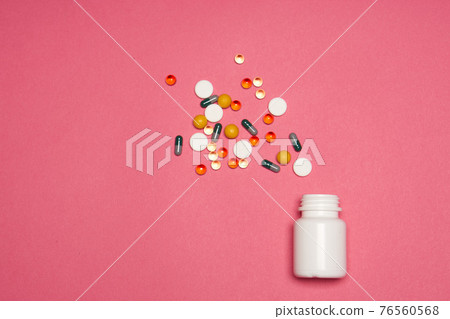 White jar with multi-colored pills on a pink background close-up 76560568