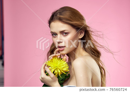 Beautiful girl with a yellow flower on a pink background nude shoulders makeup Beautiful girl with a yellow flower on a pink background nude shoulders makeup 76560724