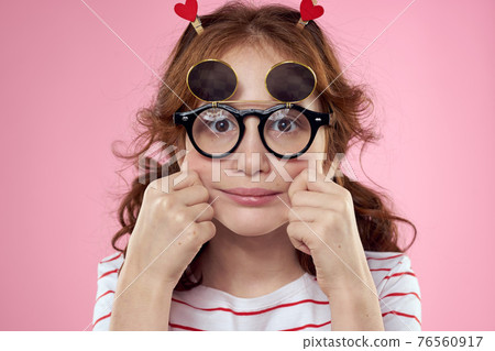 Cheerful little girl in fashionable glasses hairstyle decoration striped t-shirt pink background 76560917