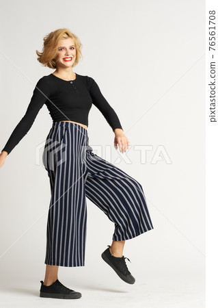 Pretty woman in black sweater striped pants fashion clothes light background studio 76561708