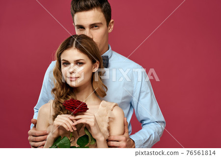 enamored man and woman with a red flower on a pink background hug each other Copy Space 76561814