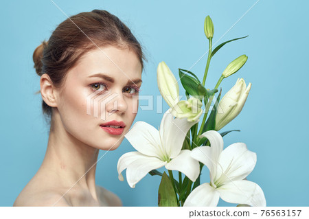 Beautiful girl with a bouquet of white flowers on a blue background cropped view naked shoulders portrait 76563157