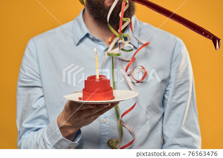 Guy with a cake in a plate on a yellow background holidays candle cropped view Guy with a cake in a plate on a yellow background holidays candle cropped view 76563476