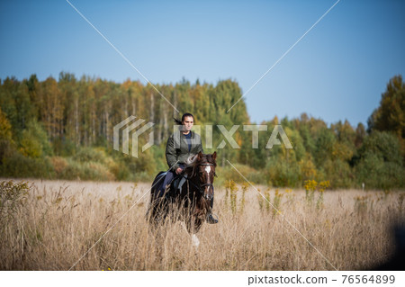 Cute girl equestrian instructor rides a horse in an equestrian club 76564899