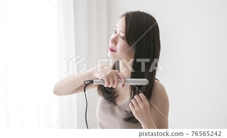 Young woman straightening her hair with a curling iron Young woman straightening her hair with a curling iron 76565242