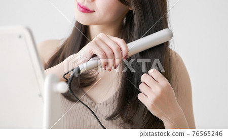 年輕女子用捲髮棒拉直頭髮 年輕女子用捲髮棒拉直頭髮 76565246
