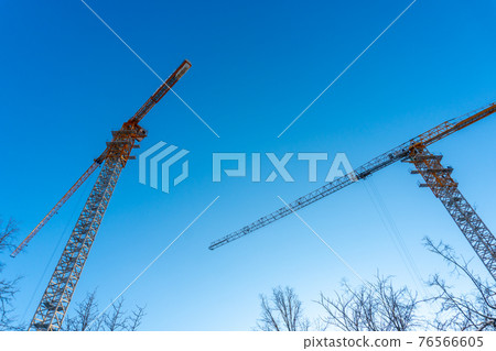 Many high tower cranes work on the construction of new homes. Two construction cranes against the blue sky. View of the two construction cranes 76566605