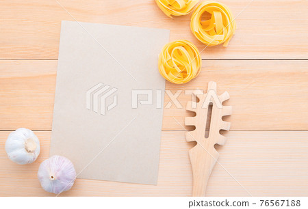 Italian foods concept and menu design . Blank paper and  pasta ladle on wooden background.Food background for tasty Italian dishes with blank brown paper and vintage pasta ladle on wooden background. 76567188