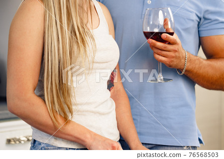 Close up of unrecognizable couple standing in kitchen with wineglass 76568503