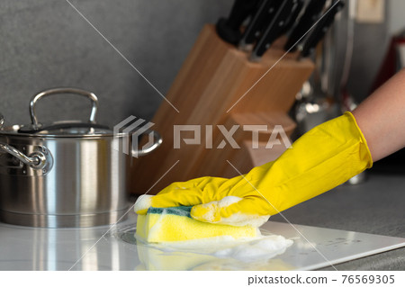 Female hands in yellow gloves cleaning electrical stove with a sponge Female hands in yellow gloves cleaning electrical stove with a sponge 76569305